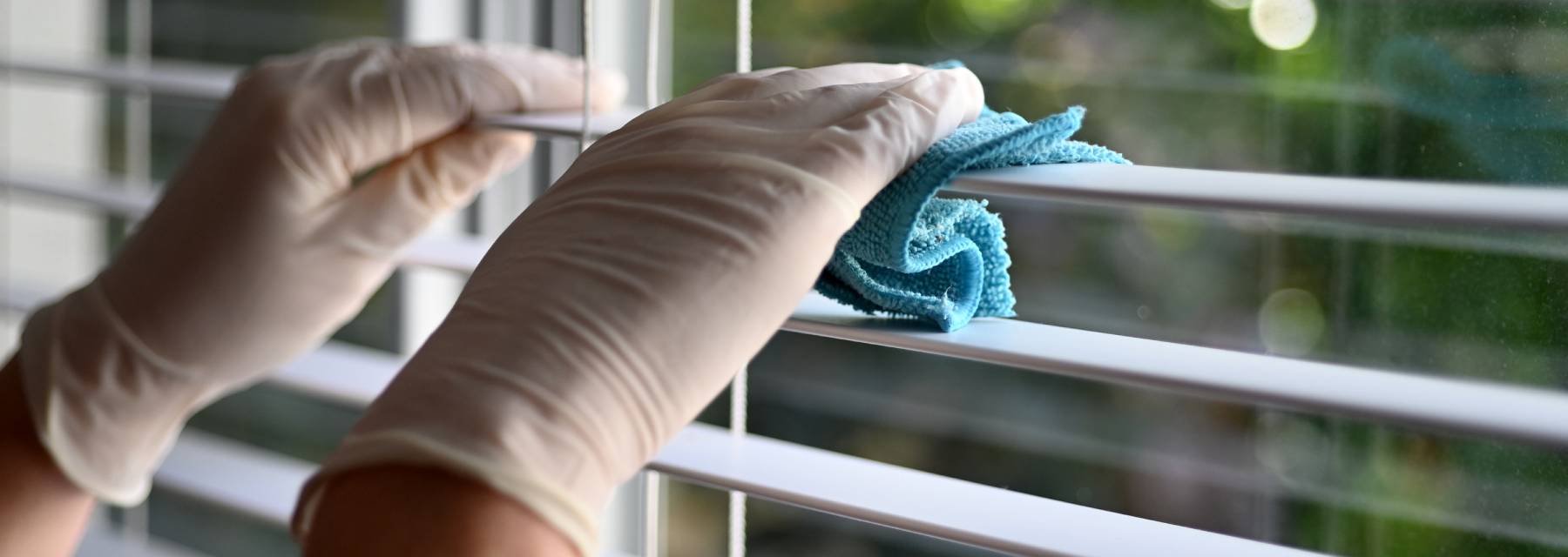 Blind cleaning technician wearing white gloves and cleaning white blinds
